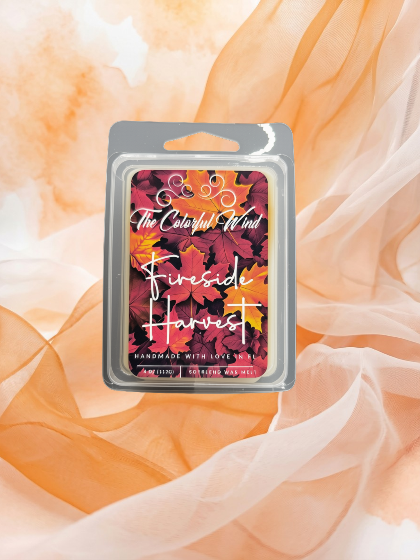A packaged wax melt or scented melt product labeled 'The Colorful Wind' and 'Fireside Harvest' with an autumn leaf pattern, placed on a soft peach fabric backdrop.