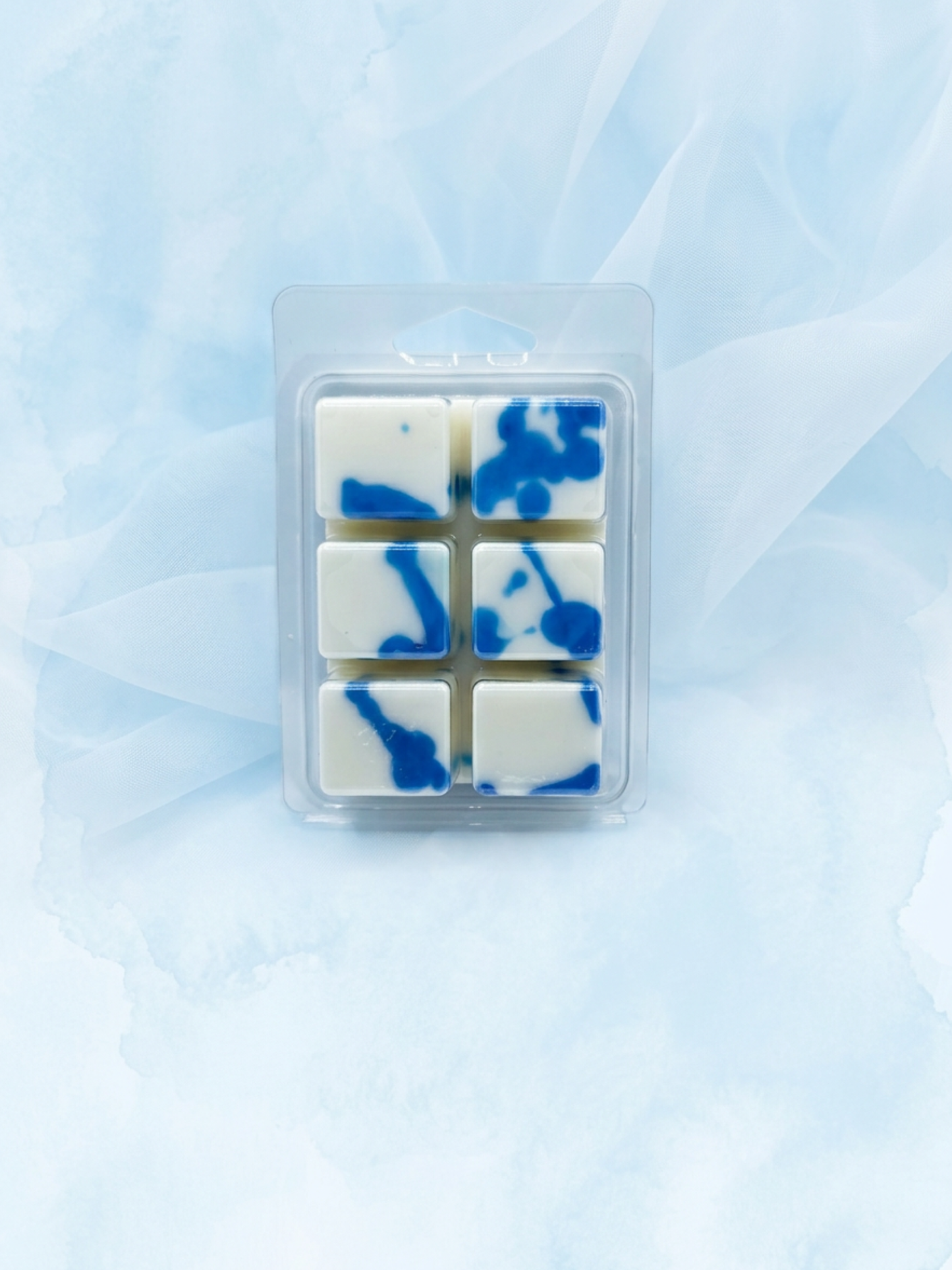 Six square white wax melts with blue marbled swirls, packaged in a clear plastic clamshell blister pack, centered on a soft light blue fabric background.