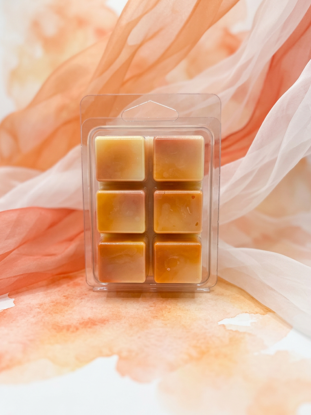 Six small square wax melts in a clear plastic clamshell package, arranged in two columns of three. The wax melts are a warm golden amber color.