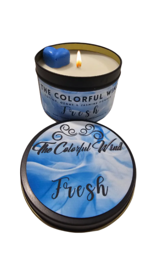 A medium-sized candle with a blue lid, labeled 'Fresh', with a lit flame in the center, providing a soothing ambiance.