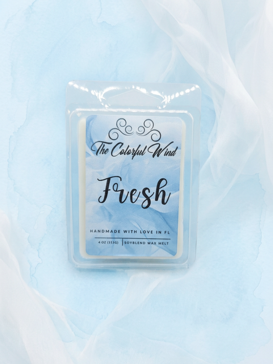 A packaged scented wax melt in a clear plastic clamshell package with a blue-and-white label reading 'The Colorful Wind Fresh' on a light blue fabric background.