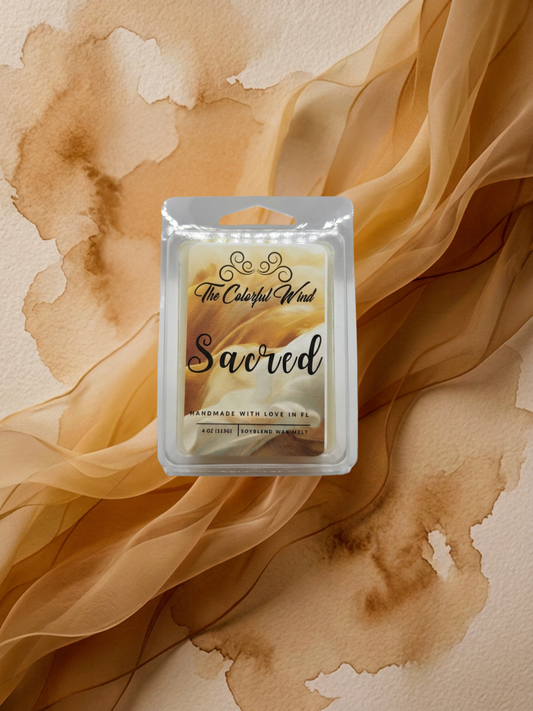 A packaged scented wax melt product labeled 'The Colorful Wind Sacred' placed on a beige surface with flowing sheer tan fabric and brown watercolor-like stains in the background.